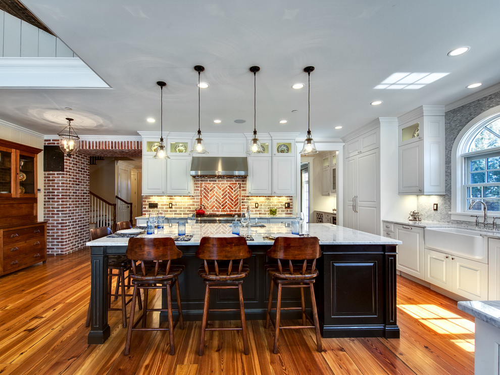 Inspiration for a large timeless l-shaped medium tone wood floor kitchen remodel in Denver with a farmhouse sink, raised-panel cabinets, white cabinets, marble countertops, paneled appliances, an island and multicolored backsplash
