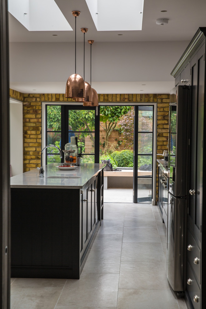 Cette photo montre une cuisine parallèle industrielle avec un évier encastré, un placard à porte shaker, des portes de placard noires, un électroménager en acier inoxydable, îlot, un sol beige et un plan de travail gris.
