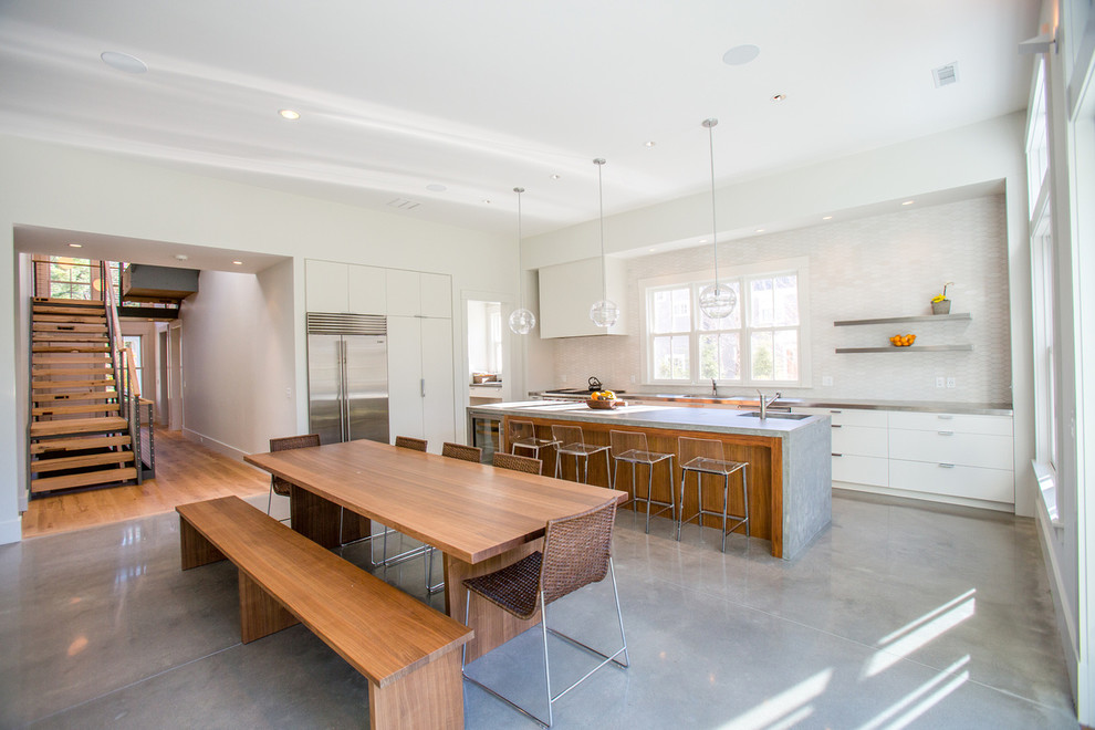 Modern inredning av ett kök, med släta luckor, vita skåp, rostfria vitvaror, betonggolv och en köksö