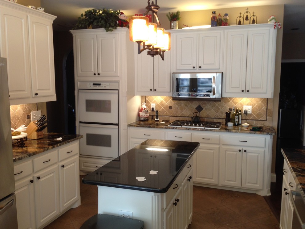 Klassisk inredning av ett kök och matrum, med luckor med upphöjd panel, vita skåp, granitbänkskiva, beige stänkskydd, rostfria vitvaror, travertin golv, en köksö, en enkel diskho och stänkskydd i stenkakel