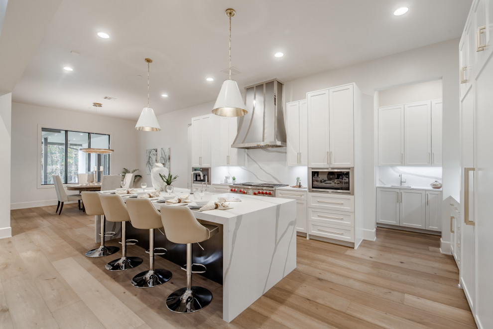 Expansive traditional l-shaped open plan kitchen in Dallas with white cabinets, engineered stone countertops, white splashback, engineered quartz splashback, integrated appliances, an island, white worktops, a submerged sink, shaker cabinets, light hardwood flooring and beige floors.