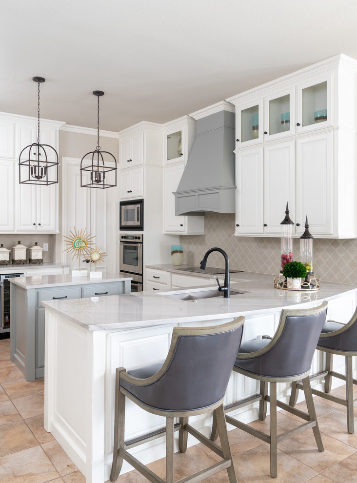 Inspiration for a transitional u-shaped beige floor kitchen remodel in Dallas with an undermount sink, raised-panel cabinets, white cabinets, gray backsplash, stainless steel appliances, an island and white countertops