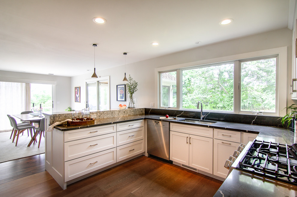 Inredning av ett modernt mellanstort flerfärgad flerfärgat kök, med en undermonterad diskho, luckor med infälld panel, vita skåp, bänkskiva i kvarts, svart stänkskydd, rostfria vitvaror, ljust trägolv, en halv köksö och brunt golv