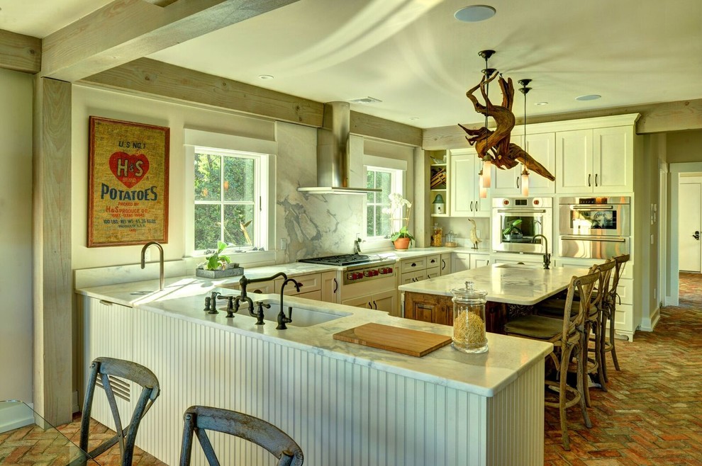 Exempel på ett stort lantligt kök, med en undermonterad diskho, luckor med infälld panel, vita skåp, marmorbänkskiva, vitt stänkskydd, stänkskydd i sten, rostfria vitvaror, tegelgolv och en köksö