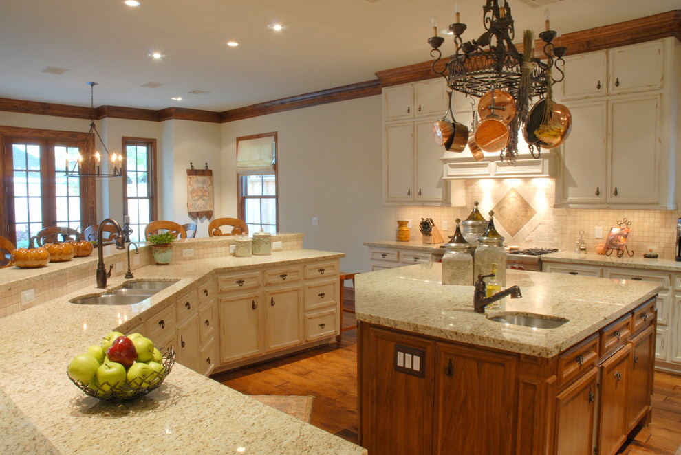 Exempel på ett klassiskt kök, med en trippel diskho, luckor med infälld panel, skåp i slitet trä, granitbänkskiva, beige stänkskydd, stänkskydd i keramik, rostfria vitvaror, mellanmörkt trägolv och en köksö