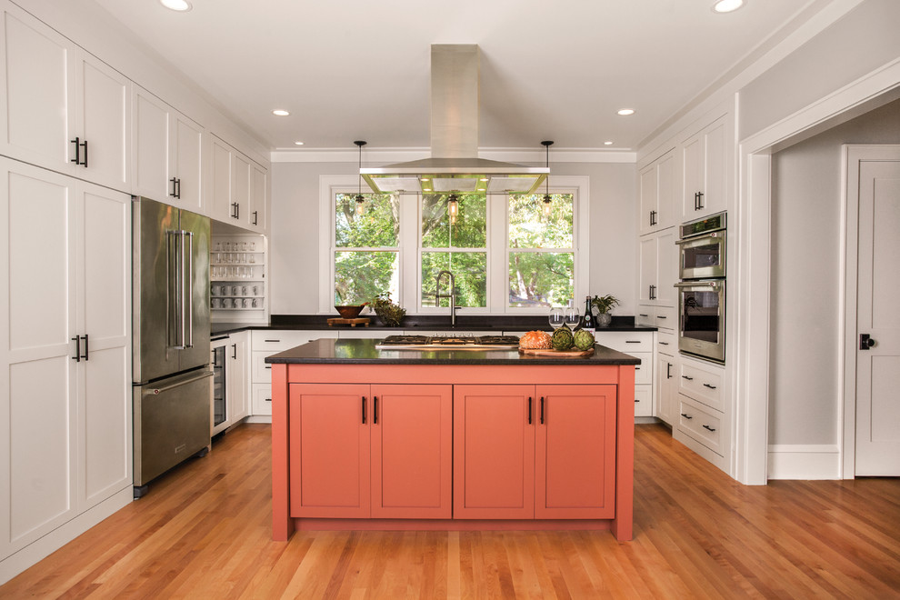 Example of a mid-sized transitional u-shaped medium tone wood floor and brown floor kitchen design in Minneapolis with shaker cabinets, orange cabinets, stainless steel appliances, an island, black countertops, an undermount sink and solid surface countertops