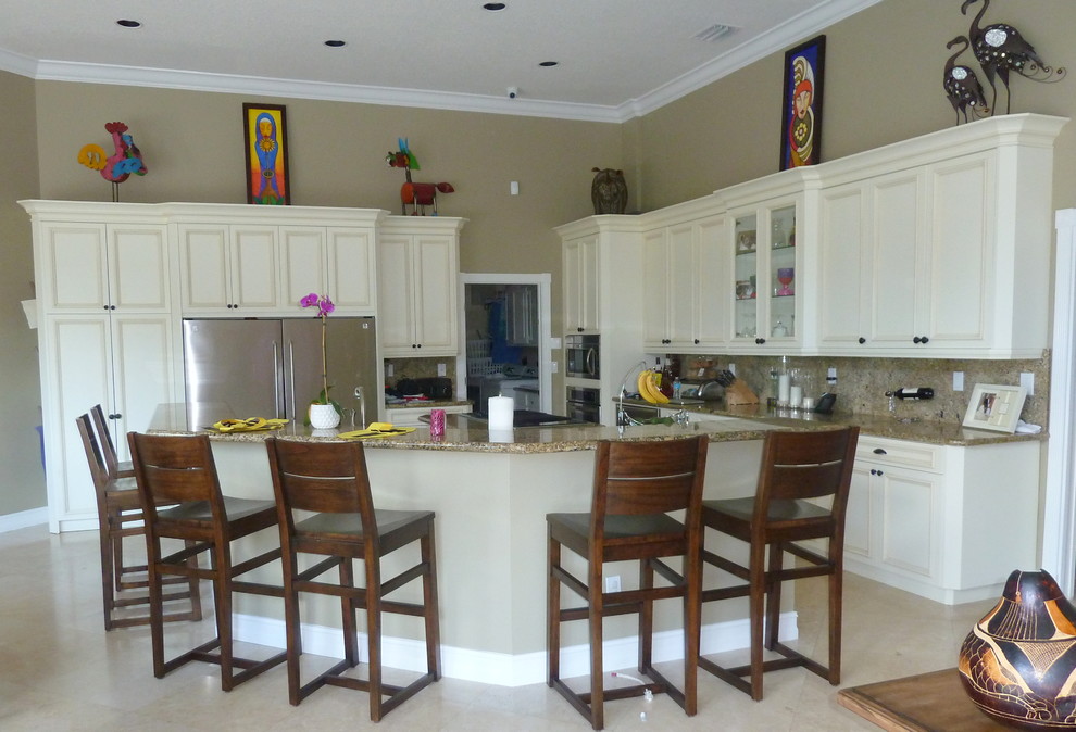 Photo of a medium sized modern u-shaped kitchen/diner in Miami with a double-bowl sink, raised-panel cabinets, white cabinets, granite worktops, brown splashback, stone slab splashback, stainless steel appliances, travertine flooring and an island.