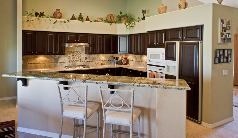 Klassisk inredning av ett kök, med luckor med upphöjd panel, bruna skåp, granitbänkskiva, flerfärgad stänkskydd, rostfria vitvaror, klinkergolv i porslin och en köksö