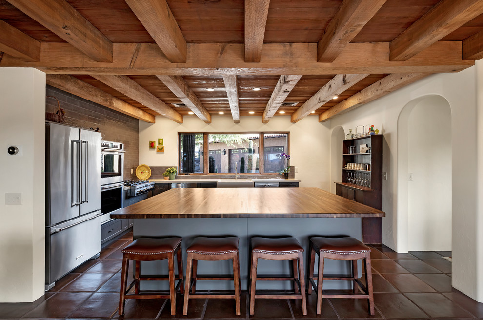 Exempel på ett stort amerikanskt brun brunt kök, med en rustik diskho, skåp i shakerstil, grå skåp, träbänkskiva, grått stänkskydd, stänkskydd i tegel, rostfria vitvaror, klinkergolv i terrakotta, en köksö och brunt golv