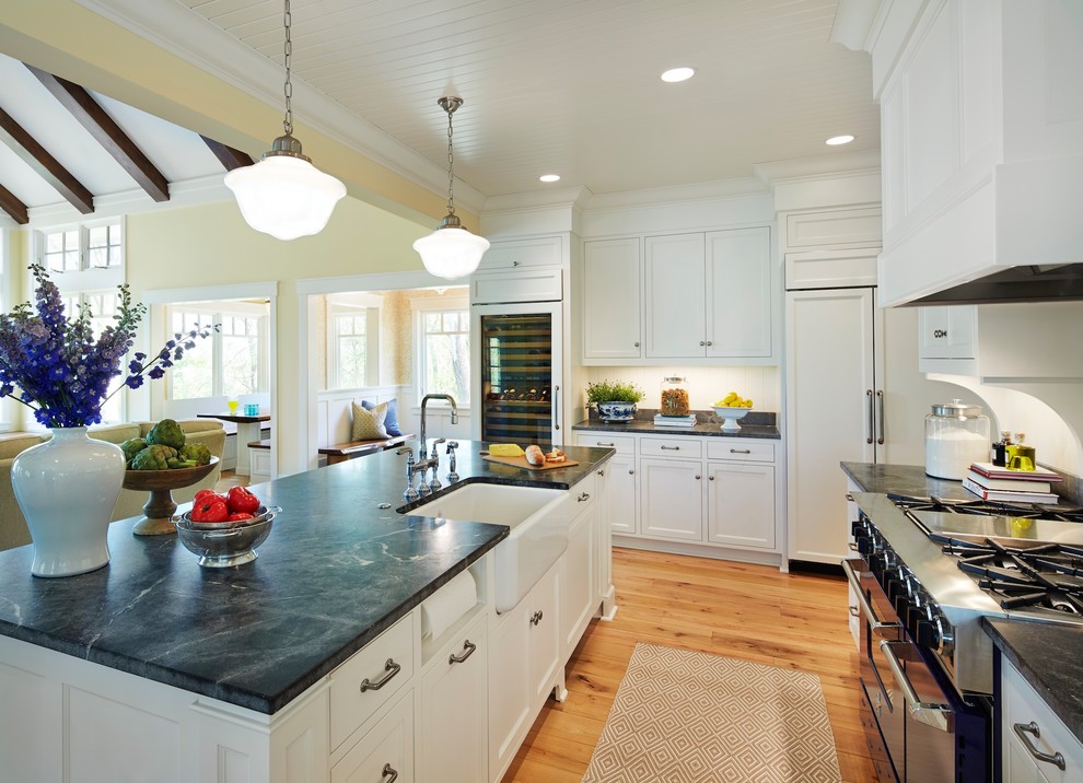 Inspiration for a large timeless galley light wood floor open concept kitchen remodel in Minneapolis with a farmhouse sink, shaker cabinets, white cabinets, soapstone countertops, white backsplash, colored appliances and an island