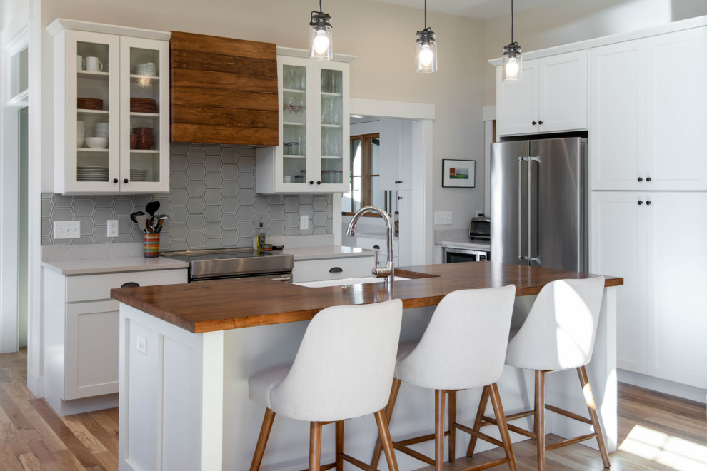 Exempel på ett rustikt brun brunt kök, med en rustik diskho, skåp i shakerstil, vita skåp, träbänkskiva, grått stänkskydd, stänkskydd i glaskakel, rostfria vitvaror, ljust trägolv, en köksö och brunt golv