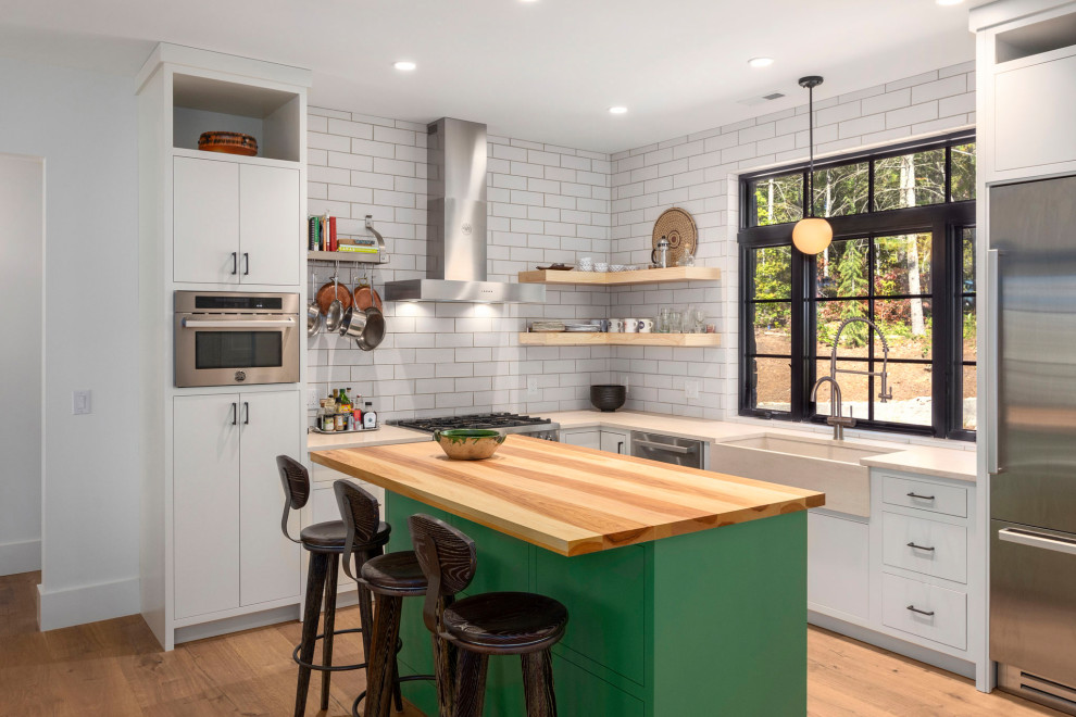 Kitchen - transitional l-shaped medium tone wood floor and brown floor kitchen idea in Other with a farmhouse sink, flat-panel cabinets, white cabinets, white backsplash, subway tile backsplash, stainless steel appliances, an island and beige countertops