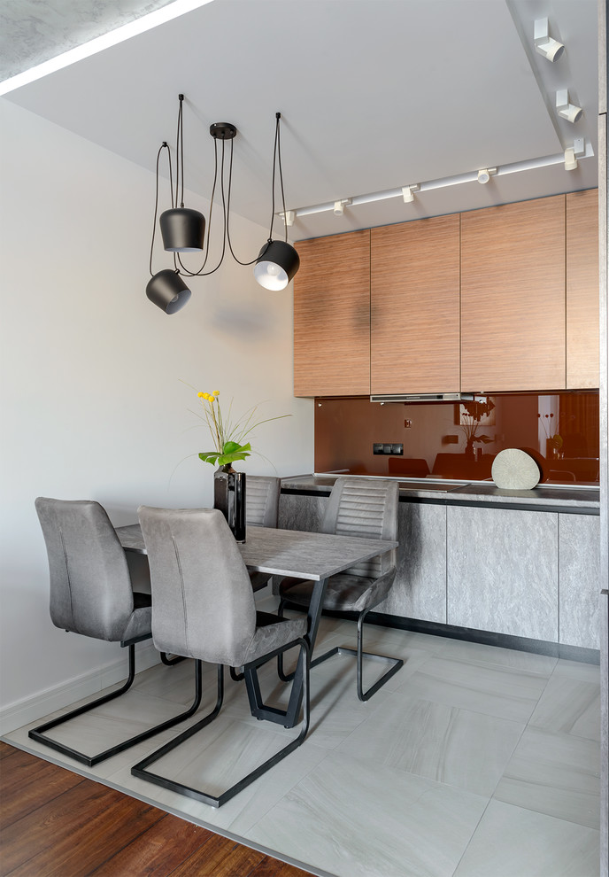 Réalisation d'une cuisine ouverte bicolore design en bois clair avec un placard à porte plane, une crédence rouge, une crédence en feuille de verre, un sol gris et un plan de travail gris.