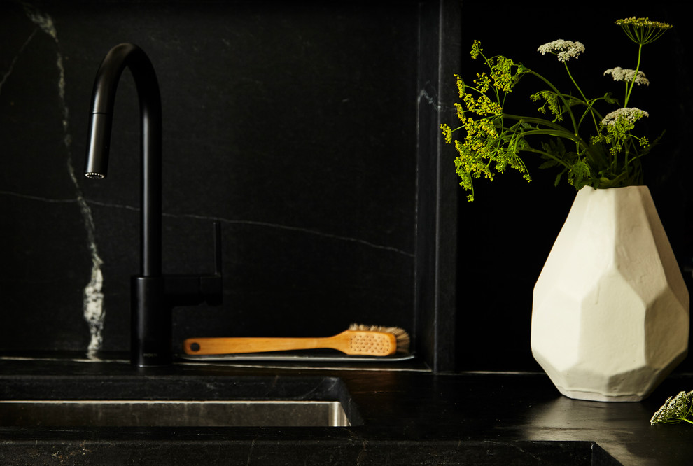 Inspiration for a contemporary kitchen in New York with an integrated sink, black splashback, stone slab splashback, stainless steel appliances, medium hardwood flooring, brown floors and black worktops.
