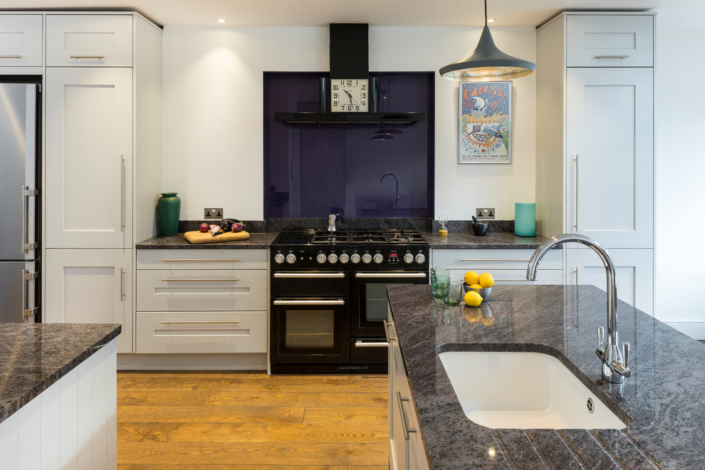 Zweizeilige, Große Moderne Wohnküche mit integriertem Waschbecken, Schrankfronten im Shaker-Stil, grauen Schränken, schwarzen Elektrogeräten, braunem Holzboden, Kücheninsel und braunem Boden in London