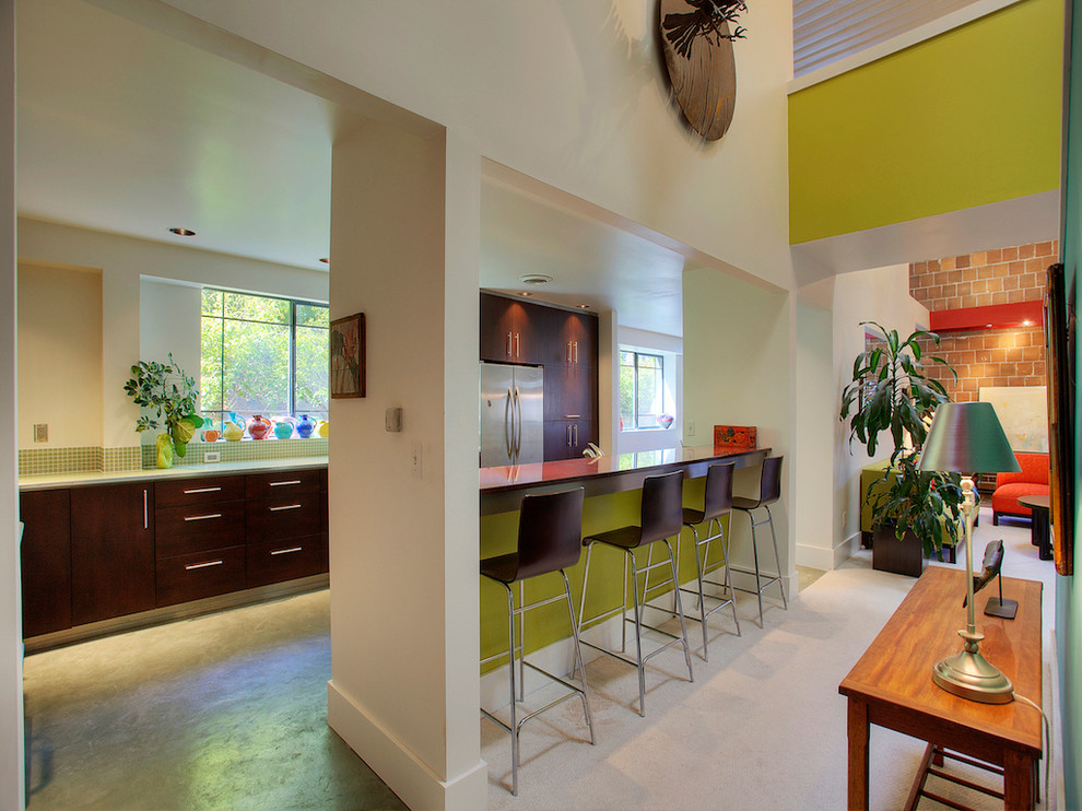 Example of a large minimalist galley concrete floor eat-in kitchen design in Seattle with a double-bowl sink, flat-panel cabinets, dark wood cabinets, glass countertops, green backsplash, glass tile backsplash, stainless steel appliances and an island