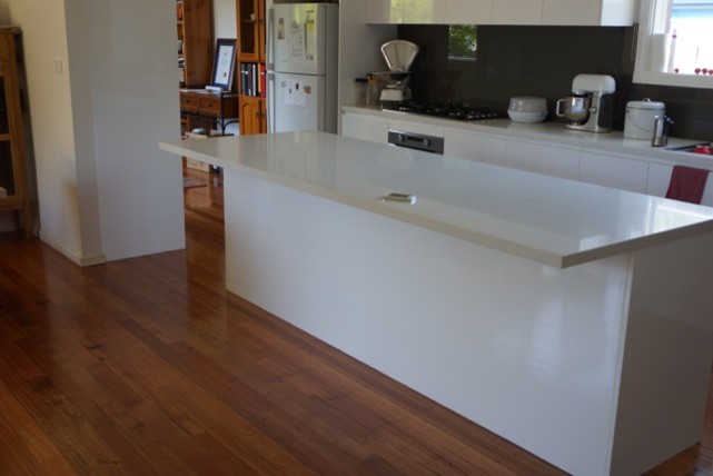 Design ideas for a large modern galley kitchen/diner in Melbourne with flat-panel cabinets, white cabinets, engineered stone countertops, black splashback, glass sheet splashback, stainless steel appliances, an island, a double-bowl sink, medium hardwood flooring and white worktops.