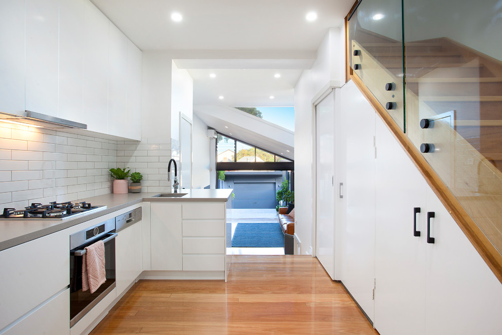 Contemporary l-shaped kitchen in Sydney with engineered stone countertops, white splashback, metro tiled splashback, stainless steel appliances, medium hardwood flooring, a submerged sink, flat-panel cabinets, white cabinets, no island and white worktops.