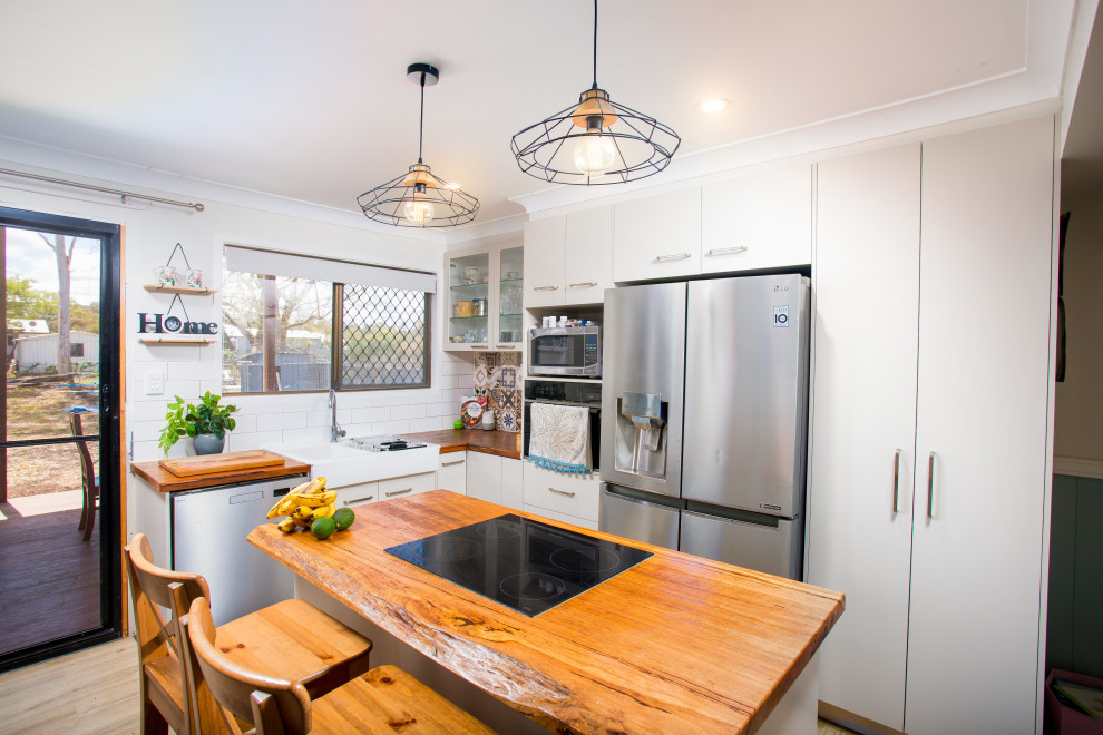 Small contemporary l-shaped kitchen/diner in Other with a built-in sink, flat-panel cabinets, white cabinets, wood worktops, white splashback, metro tiled splashback, stainless steel appliances, light hardwood flooring, an island, brown floors and brown worktops.