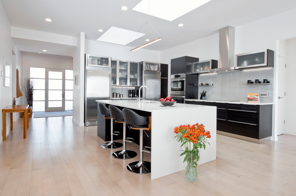 Bild på ett funkis kök, med en undermonterad diskho, luckor med glaspanel, bänkskiva i koppar, grått stänkskydd, stänkskydd i porslinskakel, rostfria vitvaror, ljust trägolv och en köksö