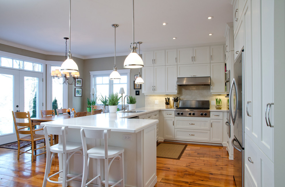 Example of a classic u-shaped eat-in kitchen design in Toronto with an undermount sink, shaker cabinets, white cabinets, quartzite countertops, beige backsplash, ceramic backsplash and stainless steel appliances
