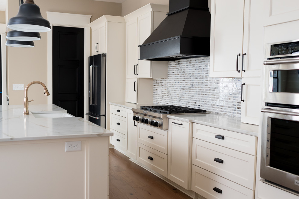Bild på ett mellanstort funkis kök, med en undermonterad diskho, skåp i shakerstil, vita skåp, flerfärgad stänkskydd, stänkskydd i tunnelbanekakel, rostfria vitvaror, mellanmörkt trägolv och en köksö