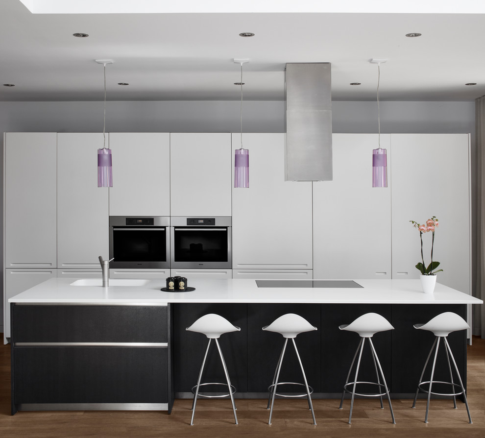 Moderne Küche mit integriertem Waschbecken, flächenbündigen Schrankfronten, weißen Schränken, Küchengeräten aus Edelstahl, dunklem Holzboden, Kücheninsel und weißer Arbeitsplatte in Toronto