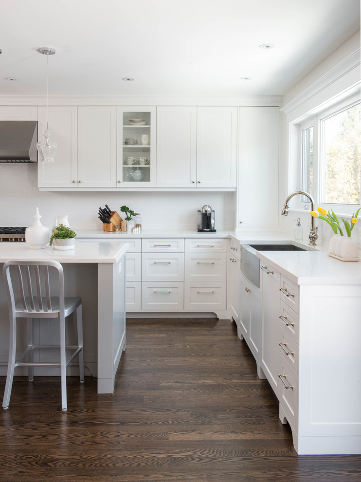 Large traditional l-shaped kitchen/diner in Toronto with shaker cabinets, white cabinets, white splashback, glass tiled splashback, stainless steel appliances, dark hardwood flooring, an island and a submerged sink.