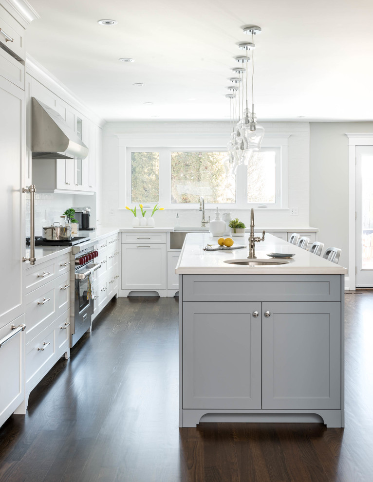 Große Klassische Wohnküche in L-Form mit Schrankfronten im Shaker-Stil, weißen Schränken, Küchenrückwand in Weiß, Rückwand aus Glasfliesen, Küchengeräten aus Edelstahl, dunklem Holzboden, Kücheninsel und Unterbauwaschbecken in Toronto