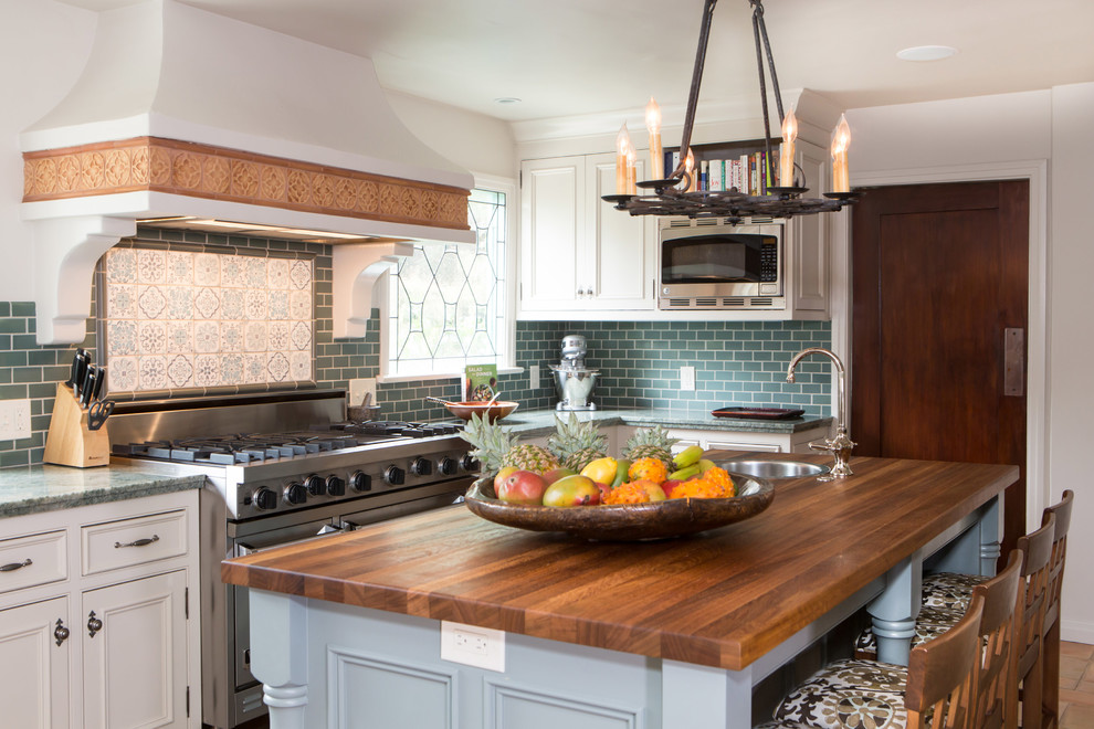 Kitchen - mid-sized mediterranean terra-cotta tile kitchen idea in Los Angeles with a drop-in sink, beaded inset cabinets, white cabinets, granite countertops, blue backsplash, ceramic backsplash, stainless steel appliances and an island