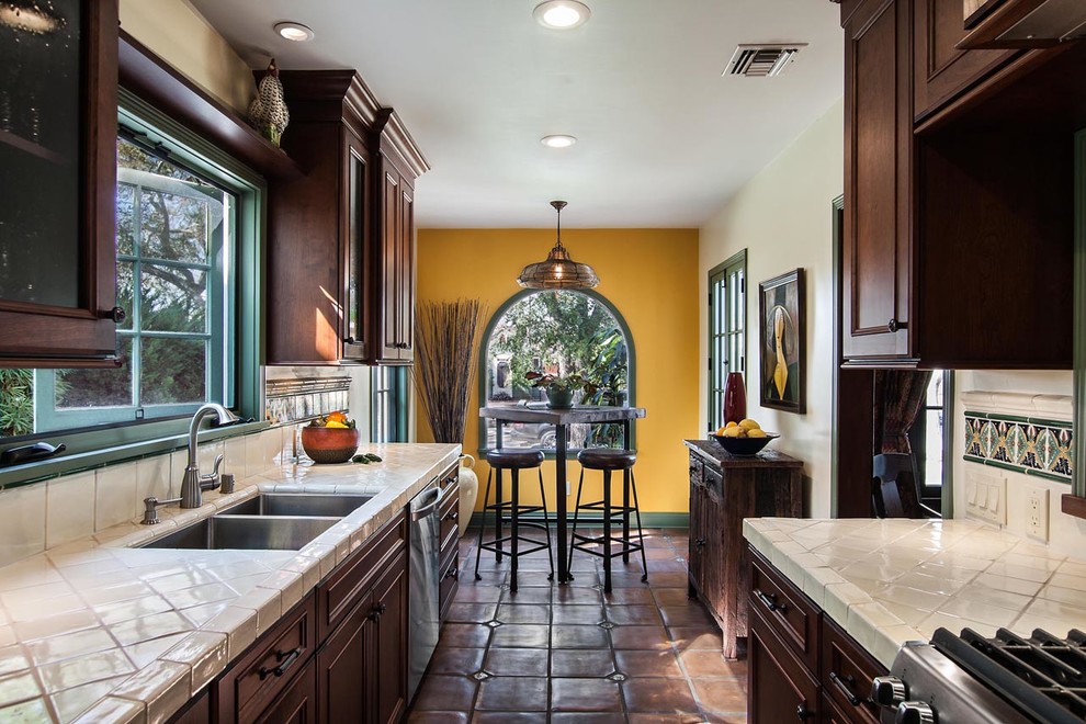 Photo of a medium sized mediterranean galley enclosed kitchen in Los Angeles with a double-bowl sink, recessed-panel cabinets, dark wood cabinets, green splashback, ceramic splashback, stainless steel appliances and ceramic flooring.