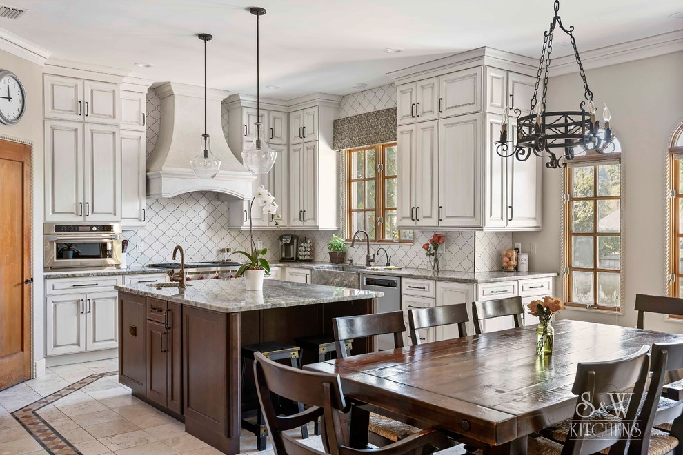 Example of a large tuscan u-shaped travertine floor and beige floor eat-in kitchen design in Tampa with a farmhouse sink, raised-panel cabinets, beige cabinets, quartzite countertops, white backsplash, ceramic backsplash, stainless steel appliances, an island and multicolored countertops