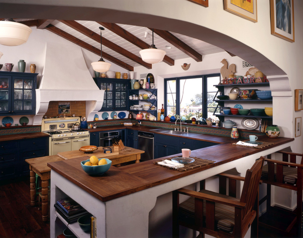 ロサンゼルスにある地中海スタイルのおしゃれなキッチン (オープンシェルフ、木材カウンター、ドロップインシンク、青いキャビネット、茶色いキッチンパネル、シルバーの調理設備) の写真