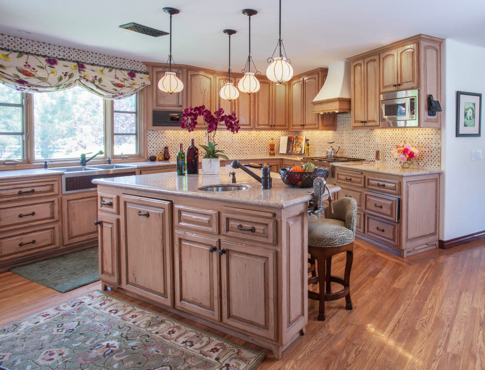 Example of a large tuscan u-shaped medium tone wood floor and brown floor kitchen design in San Diego with a farmhouse sink, raised-panel cabinets, distressed cabinets, granite countertops, multicolored backsplash, glass sheet backsplash, paneled appliances and an island