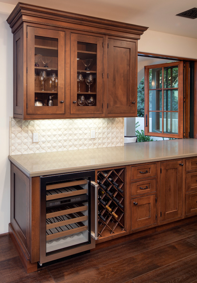 This is an example of a large mediterranean u-shaped home bar in Santa Barbara with a submerged sink, recessed-panel cabinets, medium wood cabinets, white splashback, ceramic splashback and medium hardwood flooring.