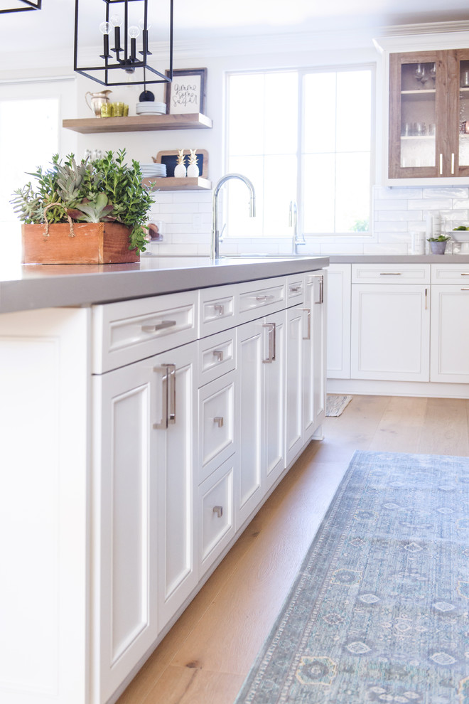 Inredning av ett klassiskt mellanstort kök, med en undermonterad diskho, luckor med infälld panel, vita skåp, bänkskiva i kvartsit, flerfärgad stänkskydd, stänkskydd i cementkakel, rostfria vitvaror, ljust trägolv, en köksö och beiget golv