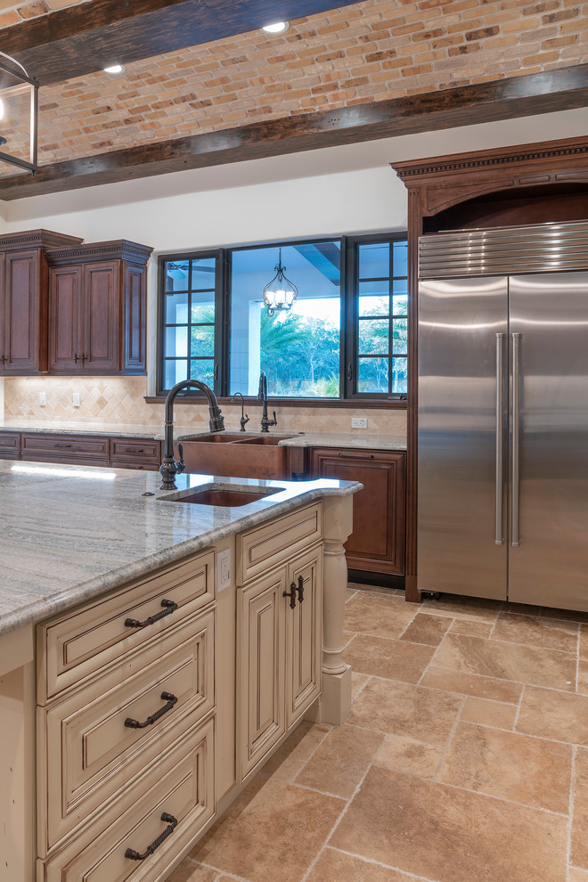 Inspiration for a large mediterranean travertine floor and beige floor kitchen remodel in Orlando with a farmhouse sink, raised-panel cabinets, dark wood cabinets, granite countertops, beige backsplash, stone tile backsplash, stainless steel appliances, an island and gray countertops
