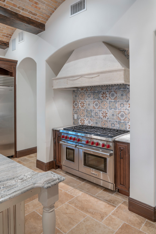 Example of a large tuscan travertine floor and beige floor kitchen design in Orlando with a farmhouse sink, raised-panel cabinets, dark wood cabinets, granite countertops, beige backsplash, stone tile backsplash, stainless steel appliances, an island and gray countertops