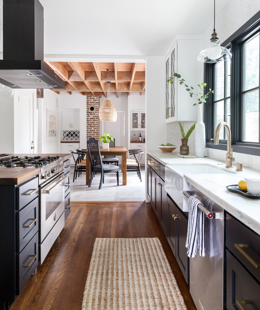 Einzeilige Wohnküche mit Landhausspüle, schwarzen Schränken, Marmor-Arbeitsplatte, Küchenrückwand in Weiß, Rückwand aus Marmor, braunem Holzboden, Kücheninsel, braunem Boden und weißer Arbeitsplatte in Sacramento