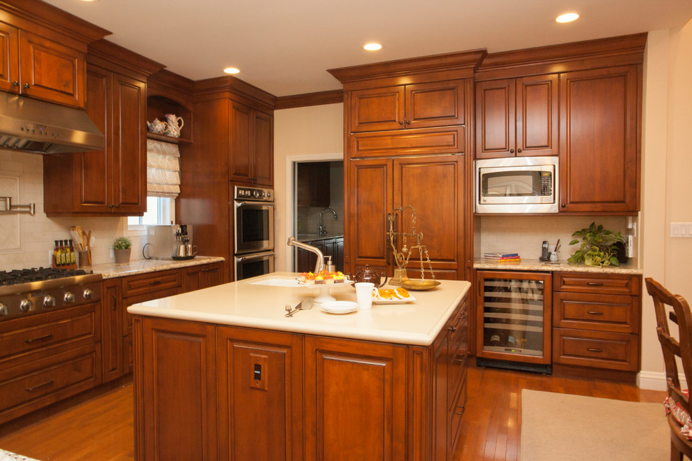 Foto på ett stort medelhavsstil kök, med en nedsänkt diskho, luckor med upphöjd panel, skåp i mellenmörkt trä, granitbänkskiva, beige stänkskydd, stänkskydd i kalk, integrerade vitvaror, mellanmörkt trägolv och en köksö