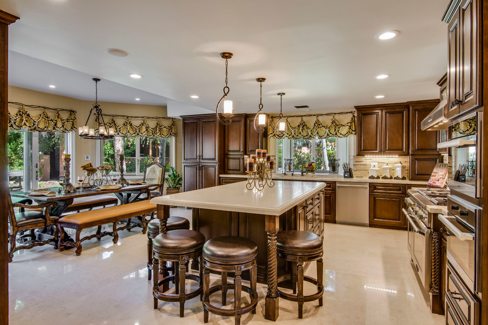 This is an example of an expansive mediterranean u-shaped kitchen/diner in Los Angeles with a built-in sink, dark wood cabinets, engineered stone countertops, beige splashback, mosaic tiled splashback, stainless steel appliances, limestone flooring and an island.