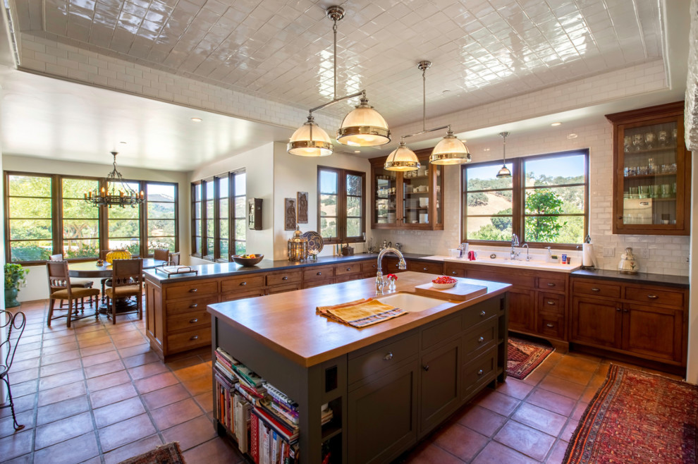 Immagine di una cucina mediterranea con lavello sottopiano, ante di vetro, ante in legno bruno, paraspruzzi bianco, paraspruzzi con piastrelle diamantate, pavimento in terracotta, pavimento arancione e top nero