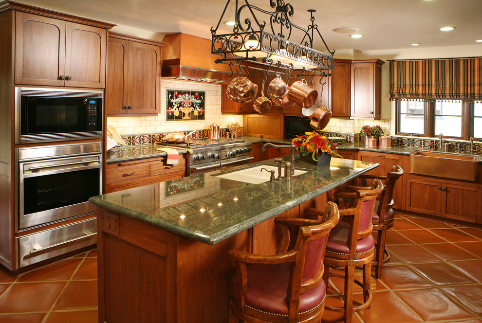 Exempel på ett stort medelhavsstil kök, med en rustik diskho, skåp i shakerstil, skåp i mellenmörkt trä, granitbänkskiva, vitt stänkskydd, stänkskydd i keramik, rostfria vitvaror, klinkergolv i terrakotta och en köksö