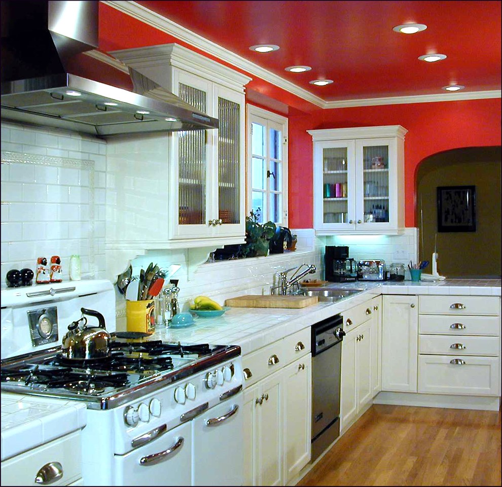 Idéer för att renovera ett mellanstort 60 tals kök, med en dubbel diskho, luckor med infälld panel, vita skåp, kaklad bänkskiva, vitt stänkskydd, stänkskydd i keramik, rostfria vitvaror och ljust trägolv