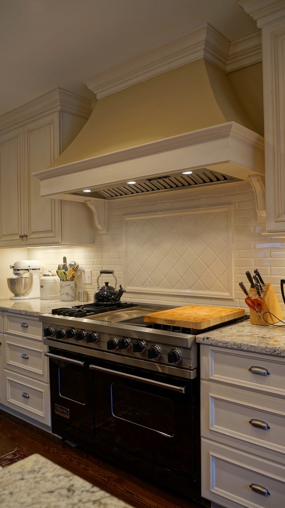 Exempel på ett mellanstort klassiskt kök, med luckor med infälld panel, granitbänkskiva, vitt stänkskydd, stänkskydd i tunnelbanekakel, rostfria vitvaror och mellanmörkt trägolv