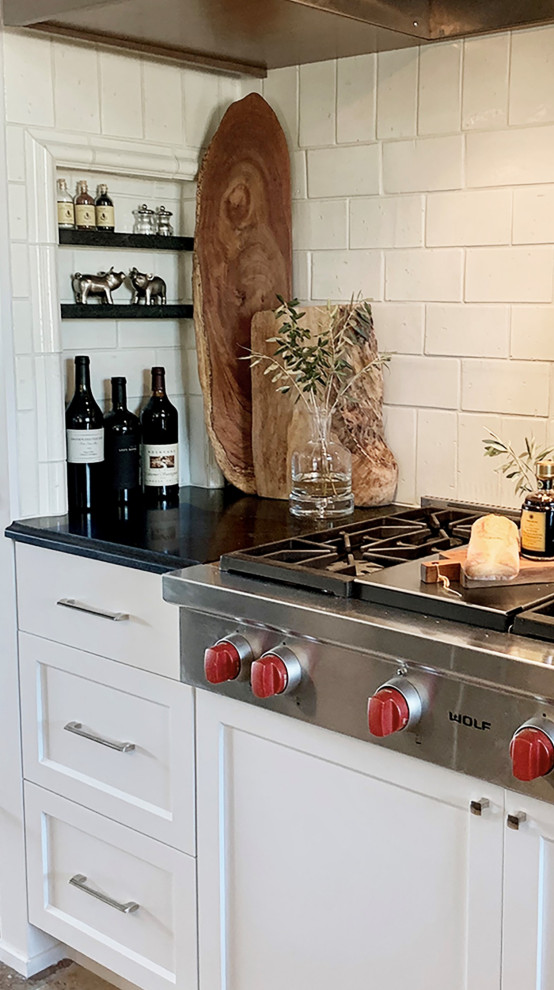 Idéer för att renovera ett stort vintage svart svart kök, med en integrerad diskho, luckor med infälld panel, vita skåp, granitbänkskiva, vitt stänkskydd, stänkskydd i keramik, rostfria vitvaror, kalkstensgolv, en köksö och beiget golv