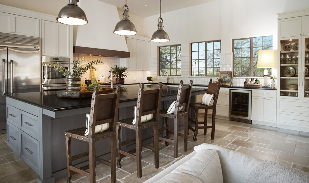 Eat-in kitchen - large transitional l-shaped limestone floor, beige floor and coffered ceiling eat-in kitchen idea in Phoenix with white cabinets, white backsplash, stainless steel appliances, an island, black countertops, an integrated sink, recessed-panel cabinets, granite countertops and ceramic backsplash