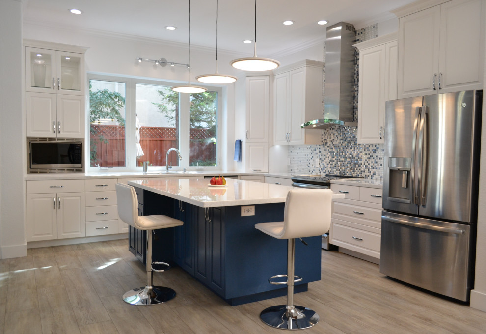 Large transitional l-shaped laminate floor and gray floor open concept kitchen photo in San Francisco with a single-bowl sink, raised-panel cabinets, white cabinets, quartz countertops, blue backsplash, mosaic tile backsplash, stainless steel appliances, an island and white countertops