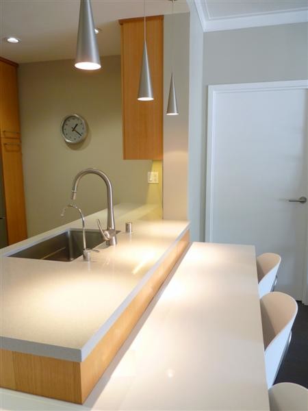 Photo of a small modern galley kitchen in San Francisco with a submerged sink, flat-panel cabinets, medium wood cabinets, engineered stone countertops, white splashback, glass tiled splashback, stainless steel appliances and a breakfast bar.