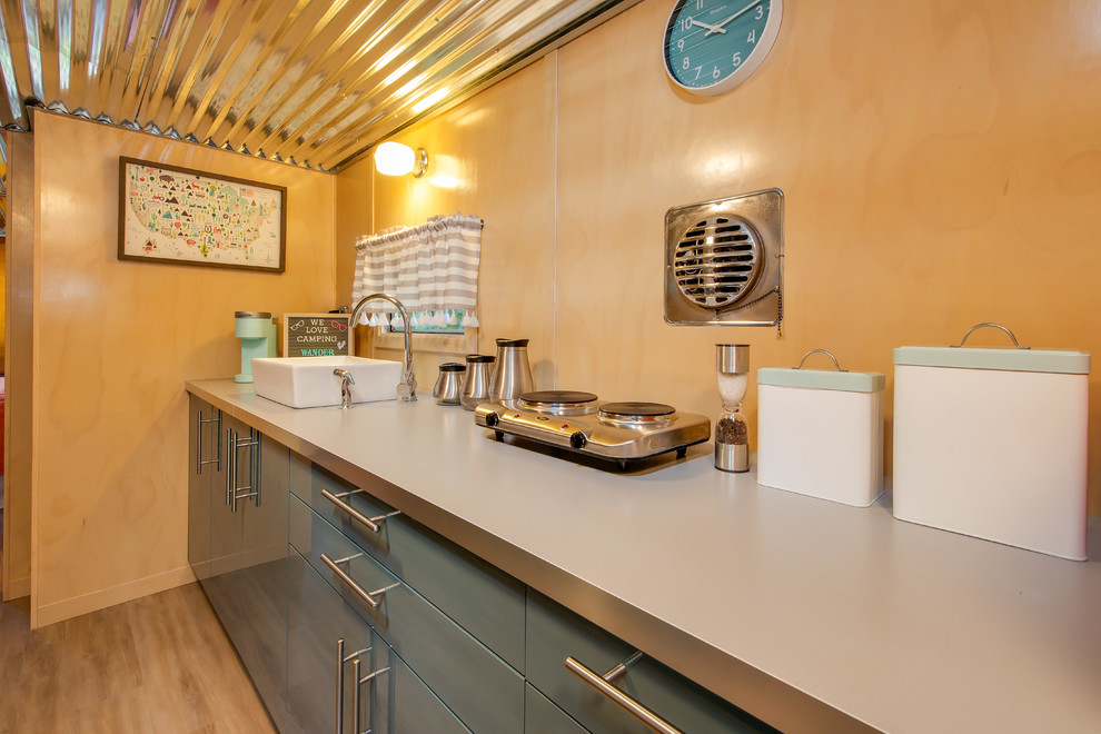 Cette image montre une petite cuisine américaine parallèle vintage avec un évier 1 bac, un placard à porte plane, des portes de placard bleues, un plan de travail en inox, un électroménager de couleur, aucun îlot, un sol beige, un sol en vinyl et un plan de travail gris.